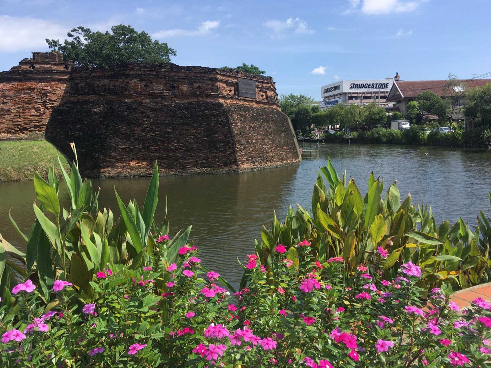 Historic brick walls of Fort of Ka Tham beside Chiang Mai's moat, with flowers along the water